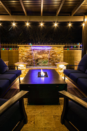 A resort style backyard at night with a waterfall, pergola, and a firepit at night.の写真素材