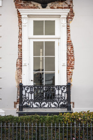 A colonial ear window with a small balcony with eroded stucco siding revealing the underlying brick...