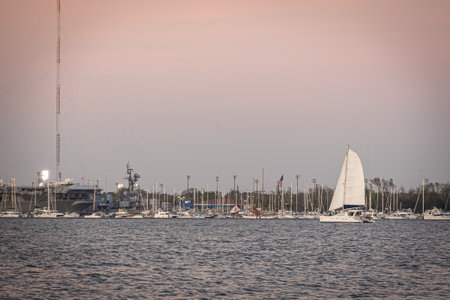 A sailboat on the open water passing a harbor with other boats docked or at anchor.の写真素材