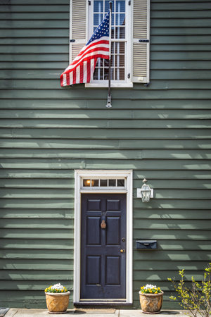 An American flag hung above the door of a colonial style home painted green in daylight.の写真素材