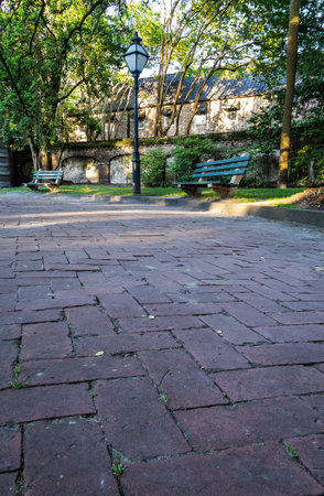 A very low angle photo of a park bench and an old fashion light with a brick sidewalk in evening light.の写真素材