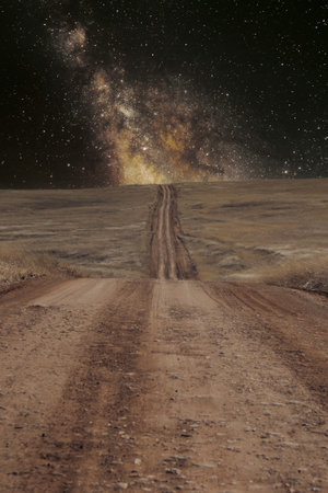 A dirt road leading off into the distance and over a distant hill on the galaxy on the horizon.の写真素材