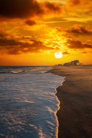 Waves of white sea foam washing up on a beach in evening light.の写真素材