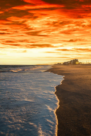 Waves of white sea foam washing up on a beach in evening light.の写真素材