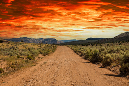 A rural dirt road leading off to distant mountains with a dramatic sunset.の写真素材