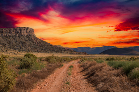 A rural dirt road leading off to distant mountains with a dramatic sunset.の写真素材