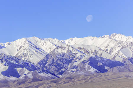 the snow covered Tianshan mountain with the moon background in Xinjiang, China on the earlier spring time.の写真素材