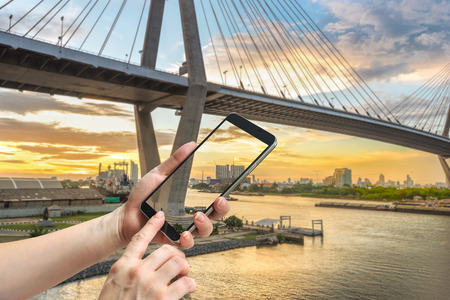 female hand hold and touch screen smart phone, on bridge blurred background.の写真素材