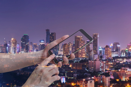 double exposure of female hand hold and touch screen smart phone, tablet,cellphone over city night light background.の写真素材