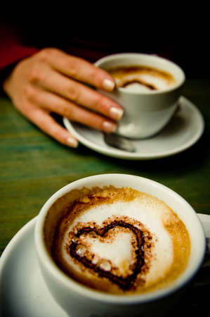 Two cups with heart shape inside them, a girl holds one cupの写真素材