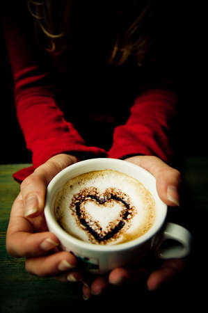 Heart shape in a cup of coffee offered by young girl
