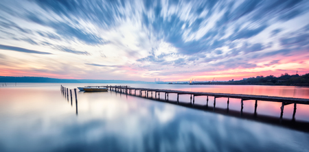 Magnificent long exposure lake sunset with boat and a wooden pier