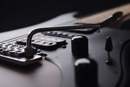 Elegant electric guitar on black background close up point of view of body details with black knobs...
