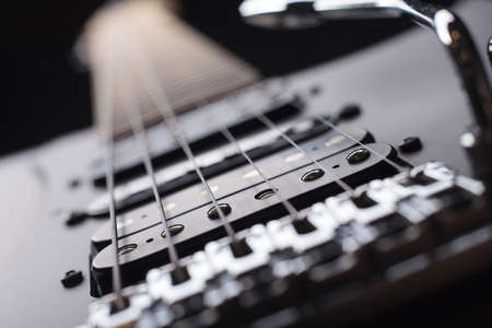 Elegant electric guitar on black background close up point of view from bridge to neck focused on...
