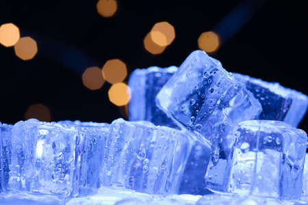 Ice cubes pile close-up with warm lights in the backgroundの写真素材