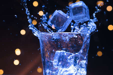 Ice splashing into a glass of waterの写真素材