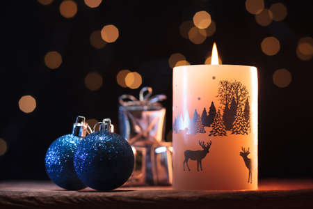 White Christmas candle, blue shiny balls and presents on a wooden table with garlands backgroundの写真素材
