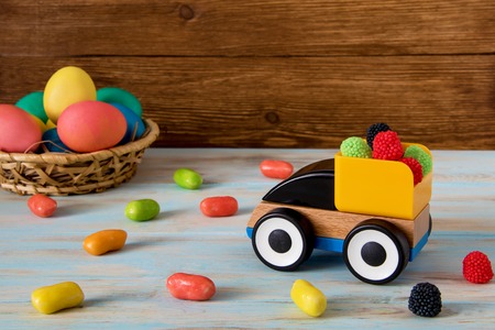 Color Easter sweets in toy track next to Color Easter eggs on wooden background and candyの写真素材