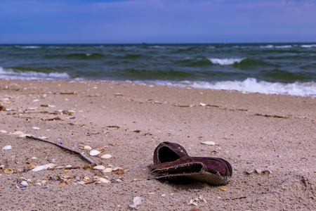 An old leather boot was taken to the sea coast by a storm in dark dayの写真素材