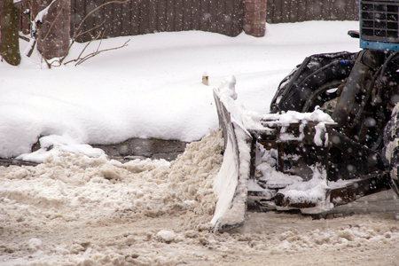 Snow removal bucket removes wet snow from the road strong snowfall in the cityの写真素材