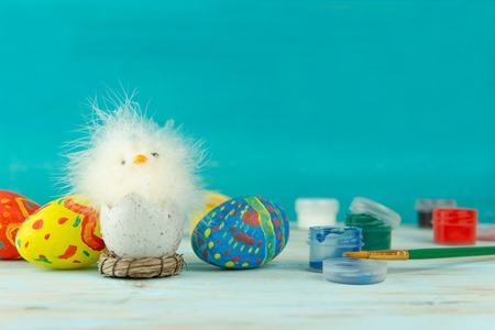 Conceptual image of Easter with baby chicken next to eggs on blue wooden background with copyspace and colored red blue green yellow paint with brushの写真素材