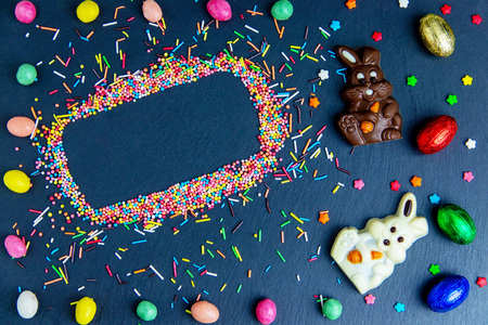 Easter greeting card with colorful candy frame and Easter egg, chocolate bunny and eggs. Top view on stone table with space for your greetingsの写真素材