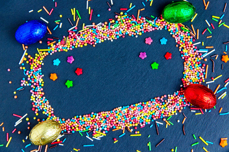Easter greeting card with colorful candy frame and Easter egg, chocolate bunny and eggs. Top view on...