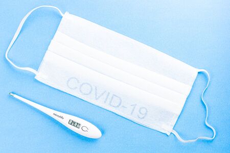 Flat lay protective medical face masks, digital thermometer with high temperature on the blue...