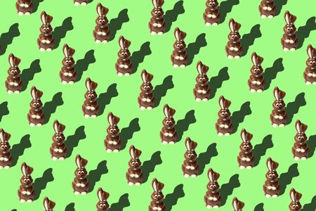 Easter bunny shaped sweets of milk chocolate laying in rows on light green background. Religious holiday composition,rabbit pattern for congratulations in greeting card. Symbol of celebration Sunday of Easterの写真素材