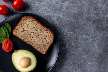 Black plate on a gray stone background with food for women red cherrys tomato, spinach, avocado and...