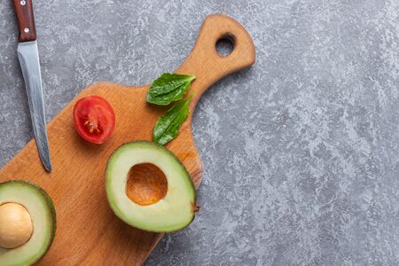 Ripe avocado cut for two parts with cherry tomato on wooden board on stone background. Tomatoes cherry, parsley and fresh green dill.の写真素材