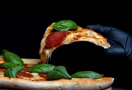 Fast food poster, chief cook takes a slice of salami pizza with spinach leaves, hands in rubber...