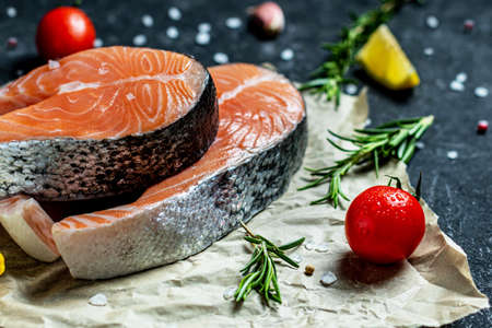 Two fresh raw salmon steaks with salt, peppers, lemon, tomatoes and rosemary on the rustic paper Creative layout made of fish, top view, flat lay, mockup, overhead. Healthy food conceptの写真素材