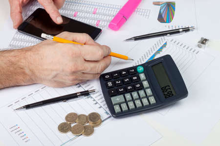 Calculating accountant interrupted by his smart phone while checking his sales dataの写真素材