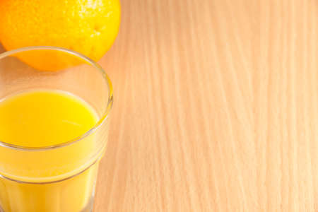 Fresh ripe whole orange and a glass of orange juice on a wooden breakfast tableの写真素材