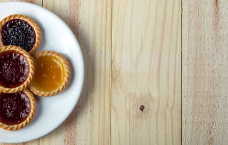 Freshly baked assorted jam tarts on a white plate on a wooden backgroundの写真素材