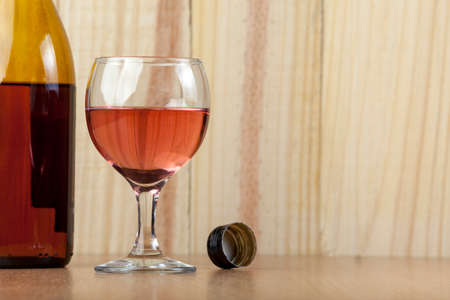 Bottle of rose wine and a poured glass with the bottle top laying on the table with a wooden backgoundの写真素材
