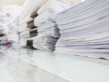 Pile of unfinished documents on office desk with businessman backgroundの写真素材