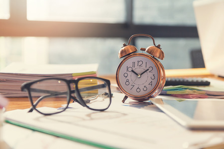 Business and finance concept of office working, Closeup clock and eyeglasses on office deskの写真素材