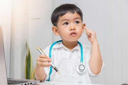 Young asian boy playing doctor and holding pen while thinking.の写真素材
