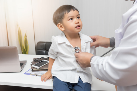 Pediatrician doctor examining a little asian boy by stethoscopeの写真素材