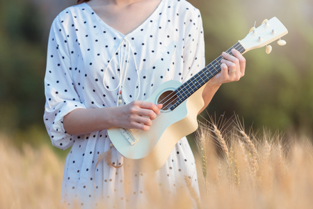 Beautiful asian woman playing ukulele and relaxing at barley field in summer on sunset timeの写真素材