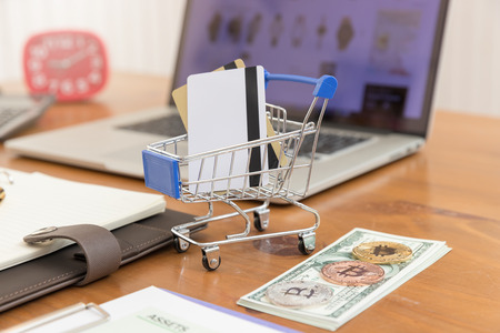 E-commerce concept, hand holding money and credit card in shopping cart with laptop open shopping website background.の写真素材