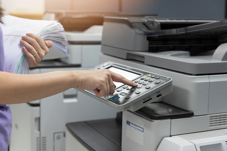 Bussinesswoman using copier machine to copy heap of paperwork in office.