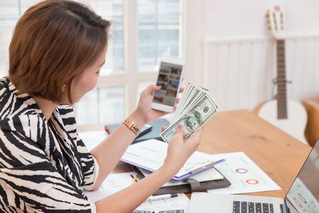 Business woman using smart phone and holding cash to shopping online in cafe.の写真素材