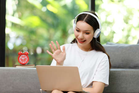 Asian woman student sitting at the table in living room,holding coffee cup and using computer laptop when studying online courseの写真素材