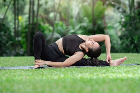 Young Asian woman practicing yoga pose at the park in morning
