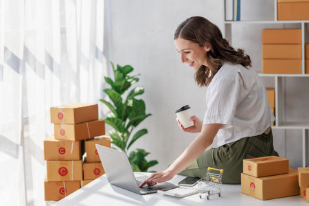 Concept of parcel delivery and selling online, Female seller or retailer using laptop to check sales of the day on online store to be packed into the parcel and ready to deliver to the customerの写真素材