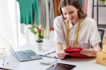 Concept of fashion and  designer,Woman fashion designer stylish with measuring tape on neck sitting working about fashion design while holding sample desing product prototype in workshop studio.の写真素材