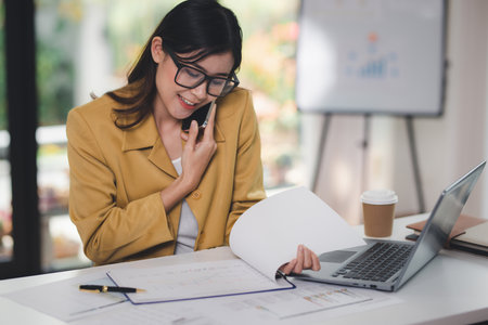 Concept of business office woman working,Businesswoman using smartphone talking to her client about invesment plan and checking  analyzing document and business investment graph data in workstation.の写真素材